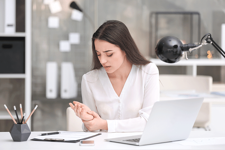 Woman at desk holding painful wrist