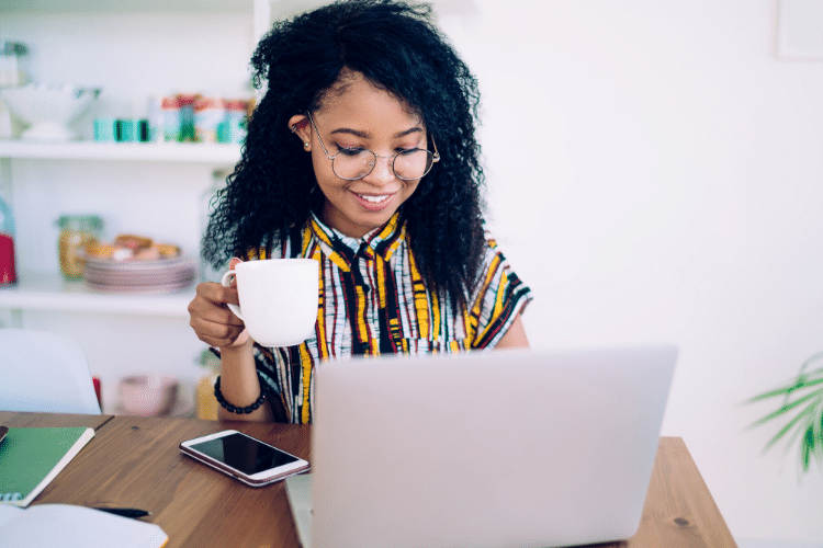 Smiling woman holding a coffee mug while looking at her laptop screen