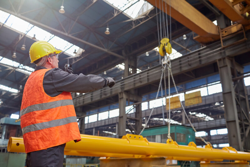 Male worker, trained by OSG, guiding hydraulic crane in factory
