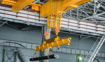 A yellow overhead crane is carrying cargo in the engineering plant shop.