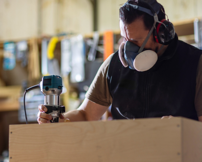 Carpenter Using Router Tool With Respirator in Woodworking Workshop